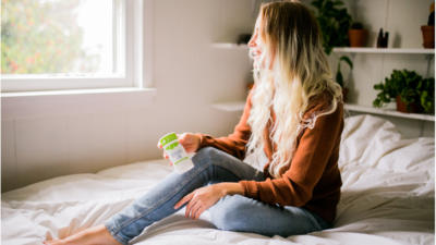 woman on bed holding schmidt's bergamot and lime deodorant looking out window